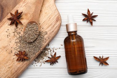 İçinde gerekli yağ şişesi, anason yıldızları, kurutulmuş tohumlar ve beyaz ahşap arka planda kaşık olan tahta.