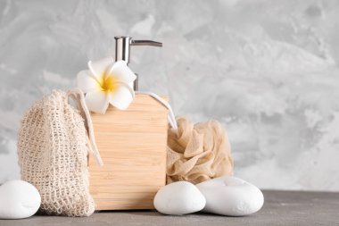 Bir şişe kozmetik ürünü, sabun torbası, banyo süngeri ve grunge arkaplanda spa taşları.
