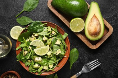 Bir kase lezzetli avokado salatası, ıspanak yaprakları ve siyah arka planda limon.