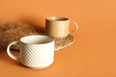 Farklı seramik kupalar, kuru sazlıklar ve turuncu arka planda hasır.