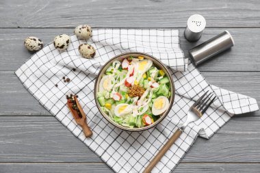 Bir kase salata ile yengeç sopası, mısır ve salatalık gri ahşap arka planda.