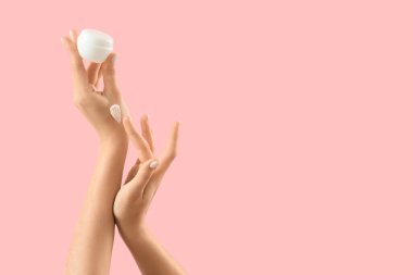 Pembe arka planda krema kavanozu olan kadın elleri