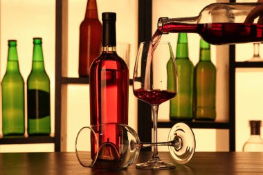 Barda şişeler olan rafların yanındaki bardaklara kırmızı şarap dökülüyor.