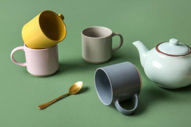 Yeşil arka planda fincanlar, çaydanlık ve kaşık kompozisyonu