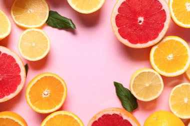 Farklı kesilmiş turunçgillerden yapılmış çerçeve ve pembe arka planda yapraklar
