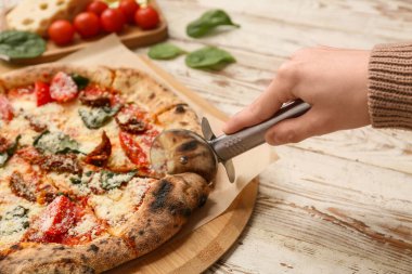 Kadın eli beyaz ahşap arka planda lezzetli bir pizza dilimi alıyor. Yakın çekim.