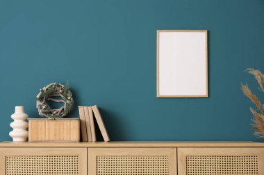 İçinde kitaplar ve vazo olan Noel çelengi mavi duvarın yanındaki klozette.