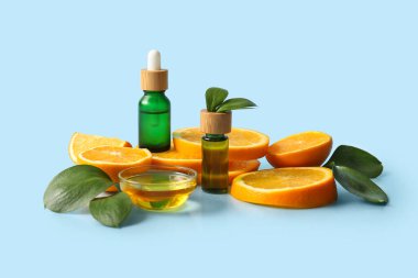 Şişeler ve cam kase portakal yağı ve mavi arka planda taze meyve dilimleri.