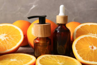 Portakal yağı şişeleri ve gri arka planda taze meyveler.