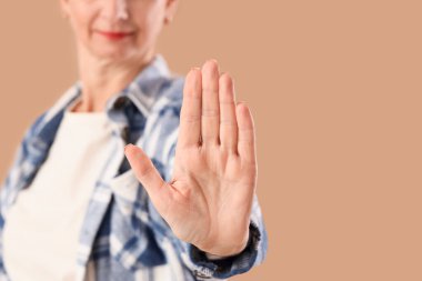 Olgun bir kadın bej arka planda DUR hareketi sergiliyor, yakın plan. Kural kavramı