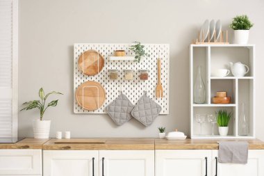 Mutfağın iç tarafındaki beyaz duvarın yanında ev bitkisi ve çatal bıçak bulunan beyaz tezgahlar.