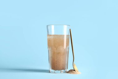 Açık mavi zemin üzerinde psyllium kabuğu olan bir bardak su.