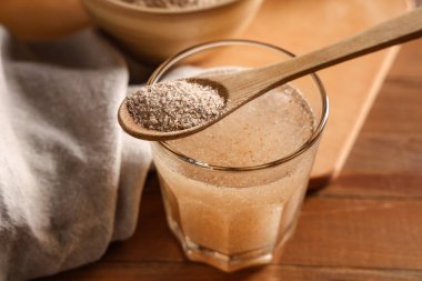 Bir bardak su ve kaşık ile ahşap zemin üzerinde psyllium kabuğu
