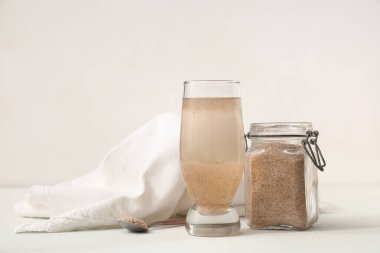 Beyaz zemin üzerinde psyllium kabuğu olan bir bardak su.