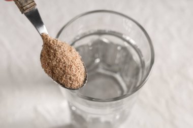 Beyaz arka planda psyllium kabuklu bir bardak su ve kaşık, yakın plan.