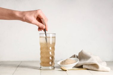 Kaşıklı bir kadın eli ve masanın üzerinde bir bardak su bulunan psyllium kabuğu.