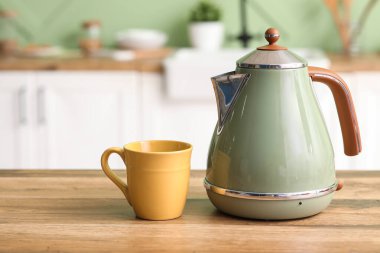 Modern yeşil elektrikli çaydanlık ve fincan mutfaktaki ahşap masada.