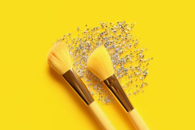 Sarı arka planda makyaj fırçaları ve parıltı darbeleri