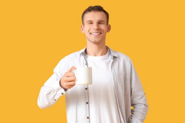 Sarı arka planda bir fincan sıcak çayı olan yakışıklı genç adam.