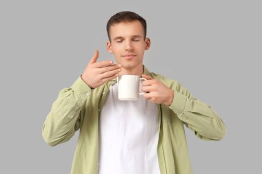 Gri arka planda çay kokusu soluyan genç adam.