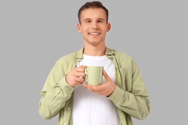 Gri arka planda bir fincan sıcak çayla gülümseyen genç adam.