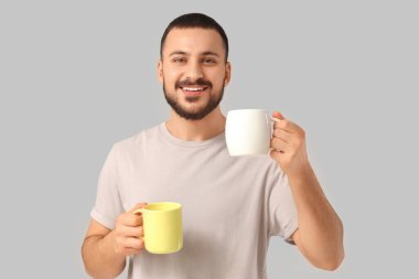 Gri arka planda sıcak çay bardakları olan yakışıklı genç adam.