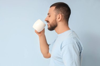 Yakışıklı genç adam mavi arka planda sıcak çay içiyor.