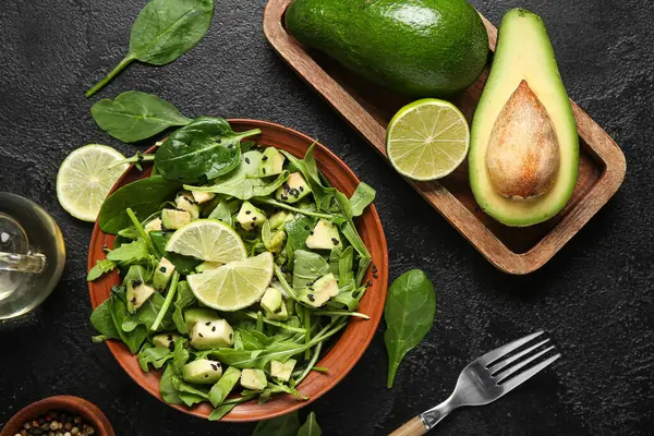 Bir kase lezzetli avokado salatası, ıspanak yaprakları ve siyah arka planda limon.