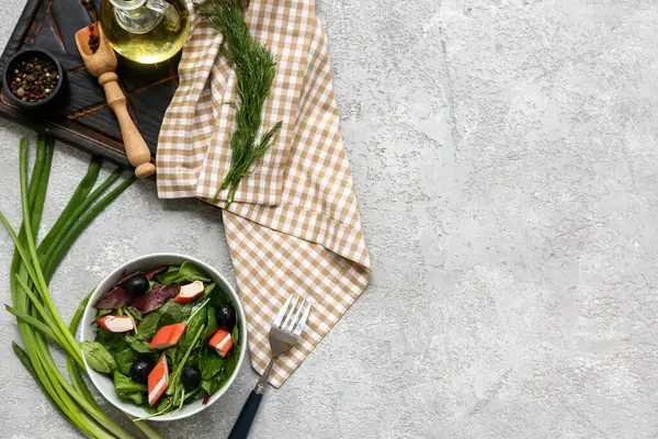 Yengeç çubuklu salata, ıspanak, siyah zeytin ve gri grunge arka planda malzemeler.