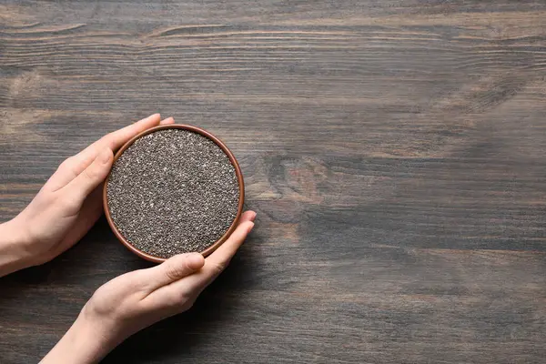 Ahşap arka planda bir kase chia tohumu olan kadın elleri.