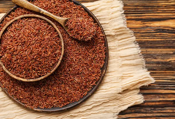 Tabak, tabak ve kaşık, ahşap zemin üzerinde çiğ kahverengi pirinç.