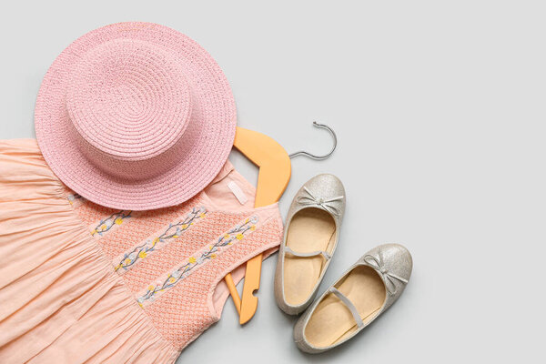 Вешалка со стильным детским платьем, шляпой и обувью на сером фоне