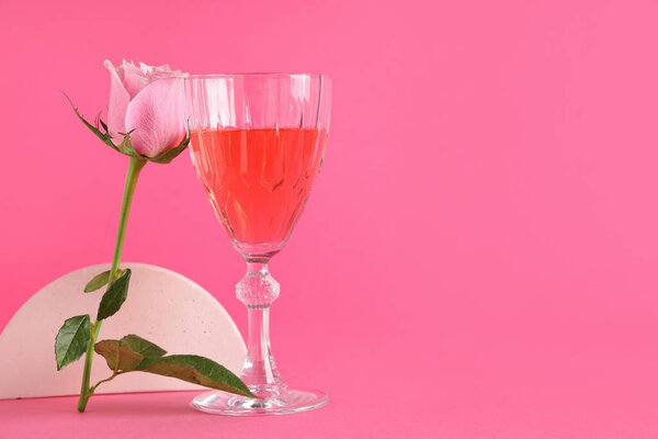Стакан розового вина и красивая роза на цветном фоне