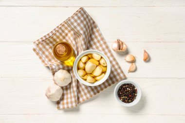 Beyaz ahşap arka planda biberli bir şişe ve bir kase taze sarımsak yağı.