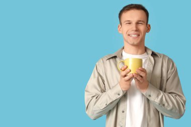 Mavi arka planda bir fincan kahvesi olan genç adam.