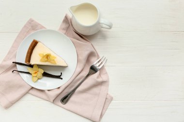 Vanilyalı tatlı peynirli kek dilimi ve beyaz ahşap arka planda çubuklar.