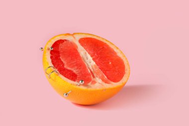 Pembe arka planda piercingli greyfurtun yarısı.