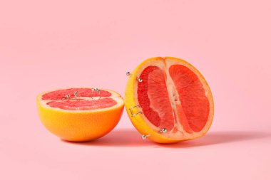 Pembe arka planda piercingli greyfurt yarıları