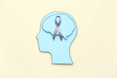 Beyni ve bej arka planda gri farkındalık kurdelesi olan kağıt insan kafası. Kanser kavramı