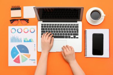 Turuncu arka planda dizüstü bilgisayarla çalışan kadın grafik tasarımcısı, üst görünüm