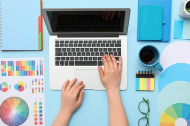 Mavi arkaplanda dizüstü bilgisayarla çalışan kadın grafik tasarımcısı, üst görünüm