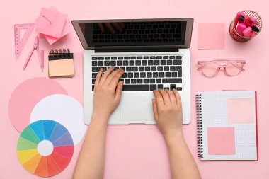 Pembe arka planda dizüstü bilgisayarla çalışan kadın grafik tasarımcısı, üst görünüm
