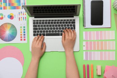 Yeşil arkaplan ve üst görünümde dizüstü bilgisayarla çalışan kadın grafik tasarımcısı