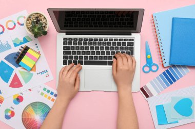Pembe arka planda dizüstü bilgisayarla çalışan kadın grafik tasarımcısı, üst görünüm