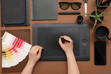 Kahverengi arkaplan üzerinde tabletle çalışan kadın grafik tasarımcısı, üst görünüm