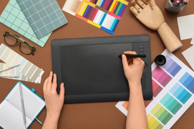 Kahverengi arkaplan üzerinde tabletle çalışan kadın grafik tasarımcısı, üst görünüm