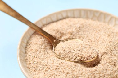 Mavi arka planda psyllium kabuk pudrası olan kase, yakın plan.