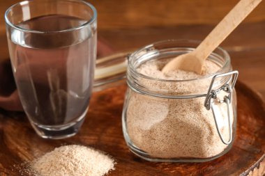 Psyllium kabuklu kavanoz ve masada bir bardak su, yakın plan.