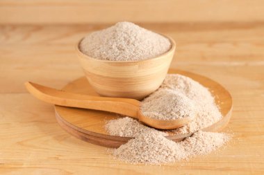 Tahta arka planda psyllium kabuğu tozu olan kase ve kaşık.