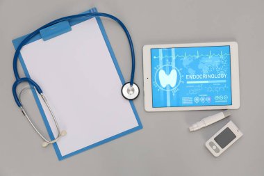 Boş klasörlü tablet bilgisayar, steteskop ve gri arka planda glukometre. Endokrinoloji kavramı